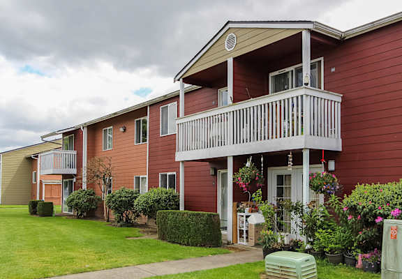 A red building with a balcony and a small garden in front.