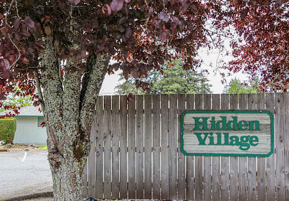 A sign that says Hidden Village is on a wooden fence.