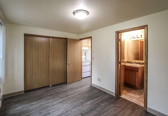 A room with a kitchen area in the back and a doorway leading to another room.