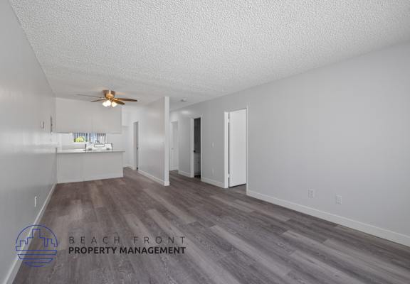 a living room and kitchen with white walls and a ceiling fan