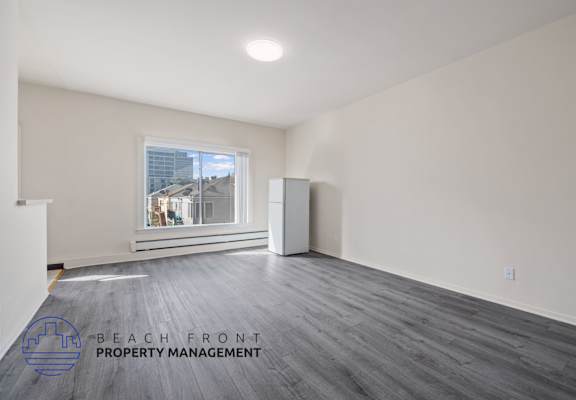 A spacious room with wooden flooring and a large window overlooking a cityscape.