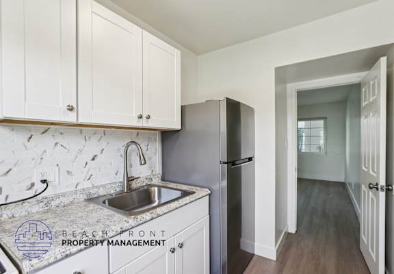 A kitchen with a sink and refrigerator with a logo for Beachfront Property Management.