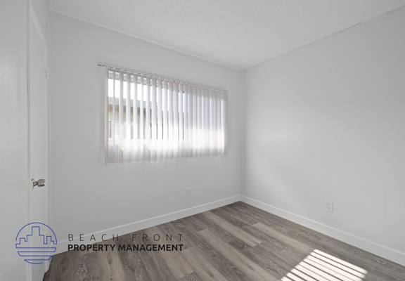 a bedroom with white walls and wood flooring and a window