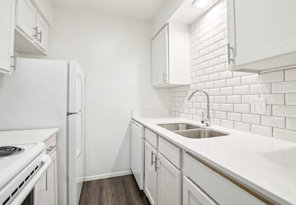 A white kitchen with a white fridge and white cabinets.