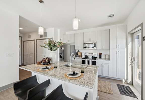 A modern kitchen with a granite countertop and black chairs.
