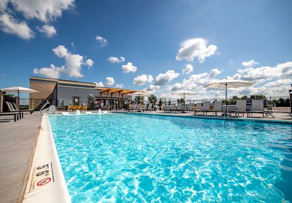 a swimming pool with umbrellas and chairs around it at The Century at Purdue Research Park-Student, West Lafayette, IN 47906