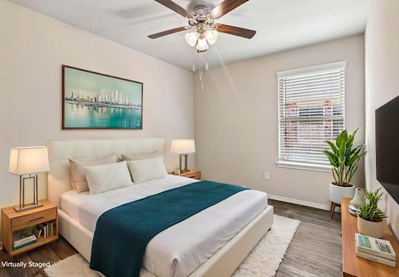 A bedroom with a bed, a ceiling fan, and a painting on the wall.