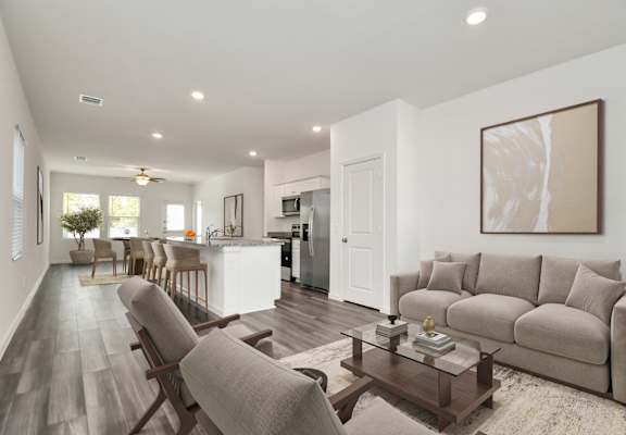 A modern living room with a grey sofa, wooden chairs, and a coffee table.