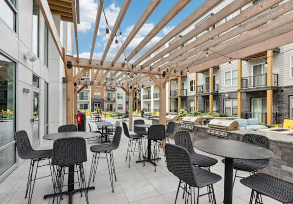 A patio with tables and chairs is covered by a wooden roof.