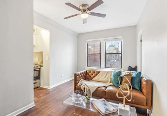 A brown couch with a tan throw blanket and blue pillows sits in a living room with a ceiling fan and a coffee table.