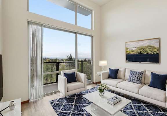 A living room with a white couch, a coffee table, and a large window with a view of the ocean.