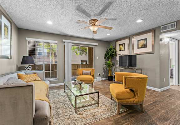 A living room with a yellow chair and a glass coffee table.