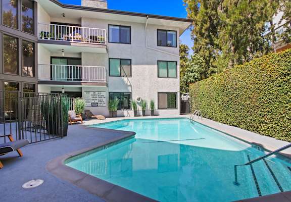 A swimming pool in front of a white building with a balcony.