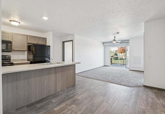 A kitchen with a black fridge and microwave, a wooden floor, and a door leading to a balcony.