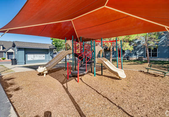 A playground with a red canopy and a slide.