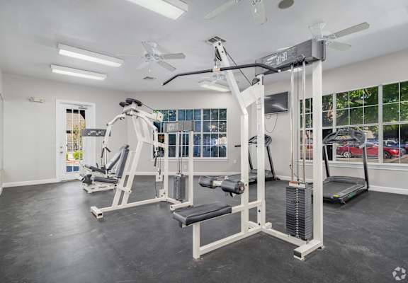 A spacious gym with a variety of equipment including a treadmill, a weight bench, and a barbell.
