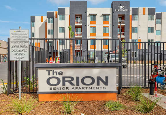 The Orion Senior Apartments is a modern building with a warning sign in front. at The Orion Senior Apartments - Orange, CA Apartments, Orange, CA, 92866