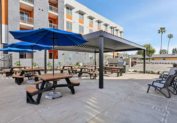 A patio with tables and chairs and umbrellas. at The Orion Senior Apartments - Orange, CA Apartments, California, 92866