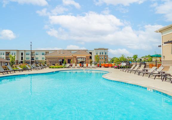 A large swimming pool in front of a building with lounge chairs around it.