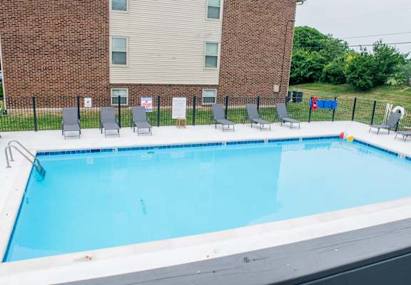 a swimming pool with chairs and a building in the background