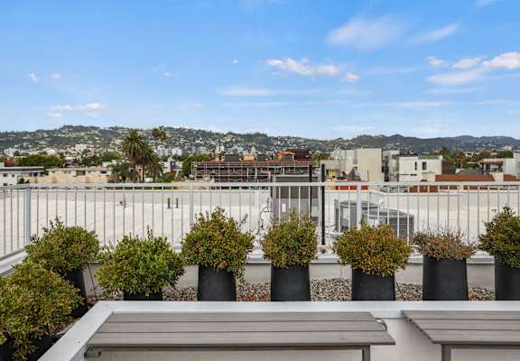 A rooftop patio with benches and potted plants overlooking a cityscape.