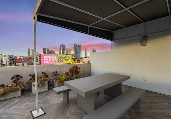 A table and benches are set up on a patio with a view of a city skyline.