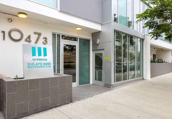 The image shows the front of a building with the number 10473 and a sign for "Wiseman" with a phone number and website.