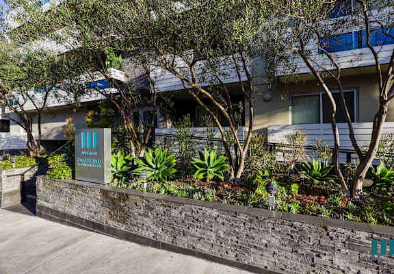a retaining wall in front of a building with trees and a sign
