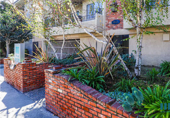 a brick retaining wall with plants in front of a building