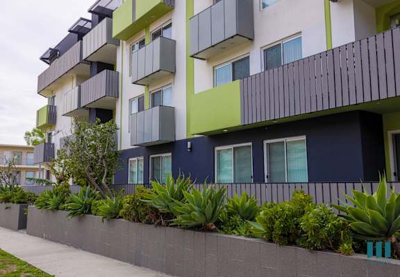 an apartment building with a sidewalk and plants in front of it