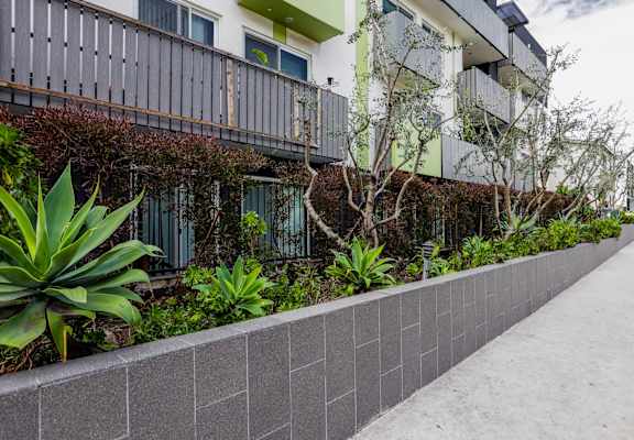 a long concrete retaining wall with plants in front of a building