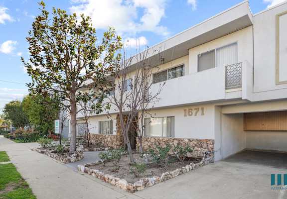 an apartment building with a sidewalk and trees in front of it