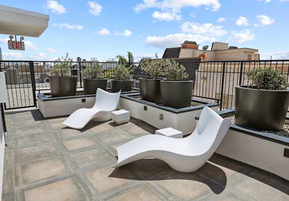 a patio with white chairs and potted plants on a roof