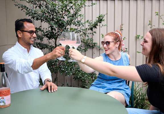 A man in a white shirt is toasting with two women at a table.