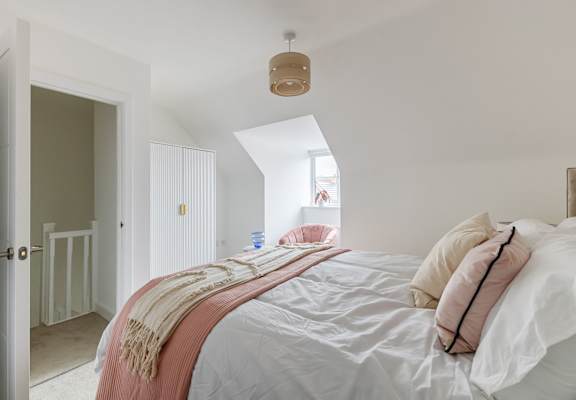 A bedroom with a bed covered in a white sheet and a pink blanket.
