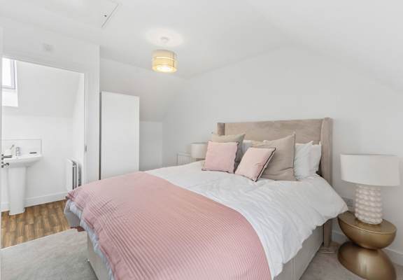 A bed with a pink comforter and a white pillow is in the center of the image.