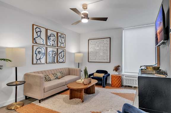 A living room with a beige couch, a wooden coffee table, and a television on the wall.