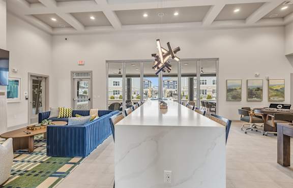 A large white marble table is in the middle of a spacious room with blue couches and chairs.