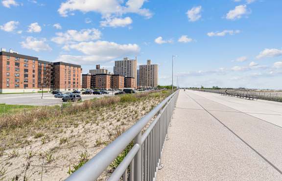 A long concrete walkway with a metal railing on the left side and a grassy area on the right side.
