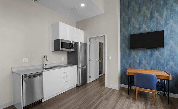 A modern kitchen with a refrigerator on the left and a grey couch in the middle of the room.