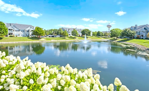 A beautiful day at the park with a pond, houses, and a water tower in the background.