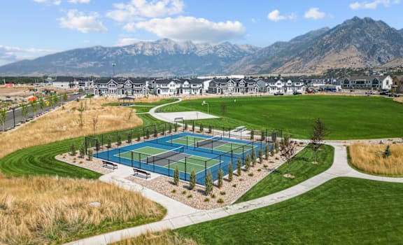 A tennis court is surrounded by a grassy area and a mountain range in the background.