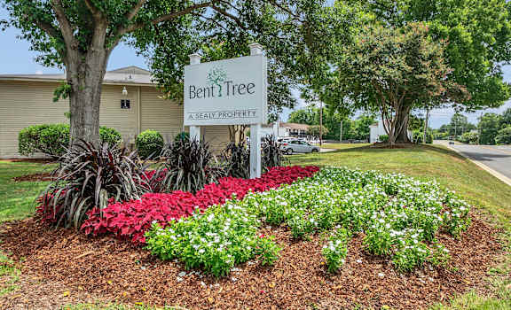 A sign that says Bent Tree stands in front of a flower bed.
