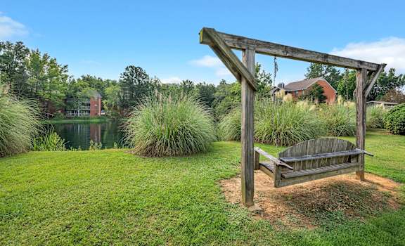 a swing bench on the grass next to a pond