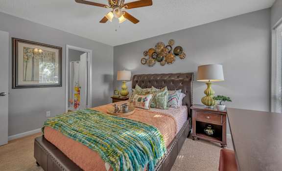 A bedroom with a bed, a ceiling fan, and a wall decoration.