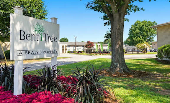A sign for Bent Tree A Sealy Property stands in front of a tree and plants.