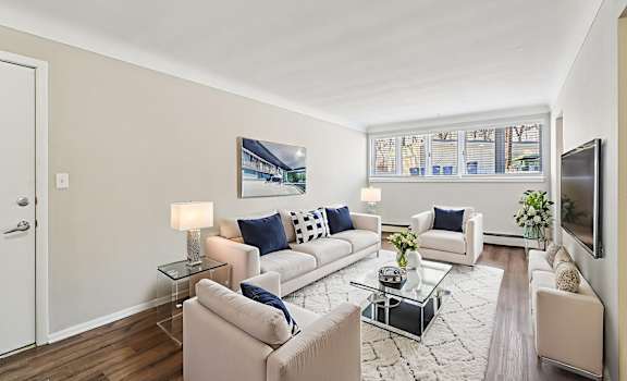 A living room with a white couch, a glass coffee table, and a flat screen TV mounted on the wall.
