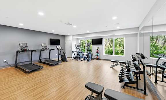 A well-lit gym with treadmills, exercise bikes, and weight benches.