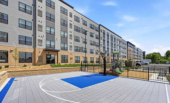 A basketball court is located in front of a multi-story apartment building.