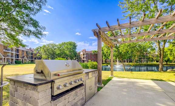 A BBQ grill is on a stone base in a sunny park.